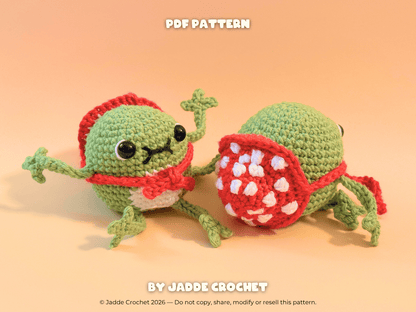 Two green crochet frogs with amanita mushroom hats on a beige background, featuring 'Jadde Crochet' branding.