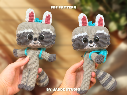 Two crocheted raccoon plush toys being held in hands, with a soft blurred indoor background. White text at the top reads 'PDF PATTERN' and text at the bottom reads 'BY JADDE STUDIO'.