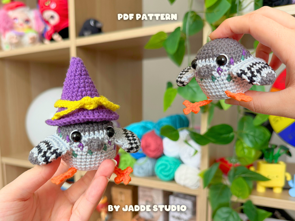 Two crocheted owl amigurumi toys are shown in a real indoor setting with shelves, plants, and yarn balls in the background. One owl wears a purple witch hat with yellow trim, and both have gray, white, black, and orange details.