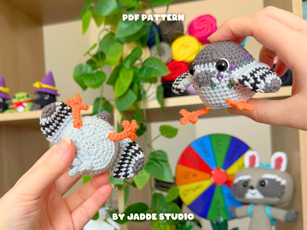 Two small crocheted bird amigurumi toys are shown in both front and back views, held in hands against a colorful indoor background with shelves, plants, yarn balls, and a wheel. Text overlays read 'PDF PATTERN' and 'BY JADDE STUDIO'.