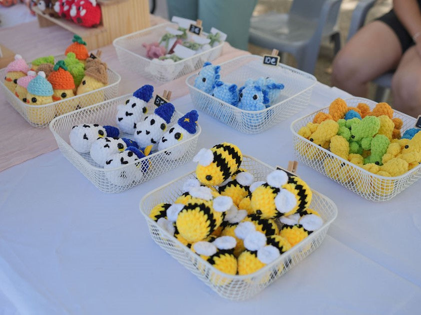 Table with baskets of colorful crocheted toys on a white tablecloth.