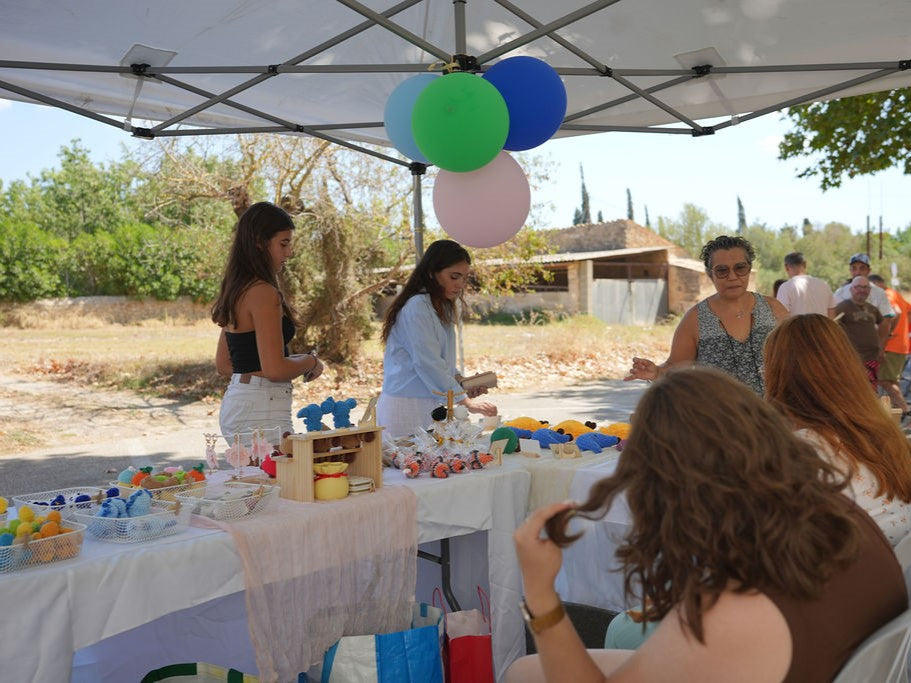 Group of people gathered under a tent with balloons and a table set up outdoors selling crochet plushies