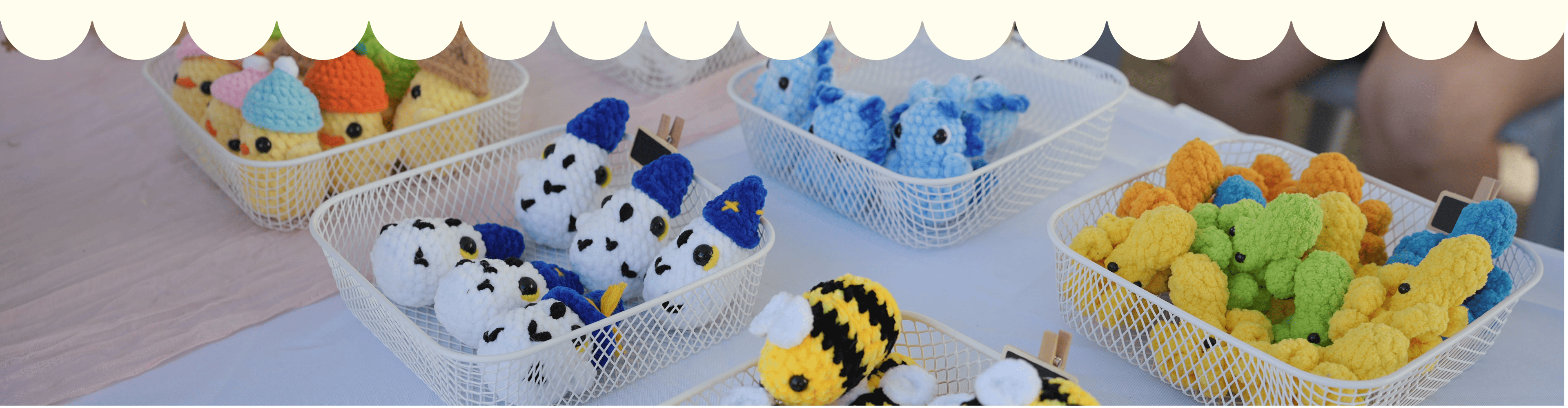 Baskets of colorful plush toys on a table with a white lace curtain in the background.
