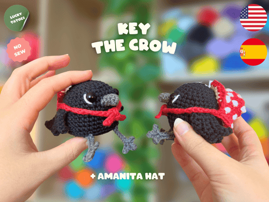 Two small crocheted crow characters wearing purple witch hats with yellow bands are held in human hands against a colorful blurred background. Text reads 'KEY THE CROW' and '+ WITCH HAT', with 'LUCKY TATTOO' and 'NO SEW' badges plus US and Spain flags.
