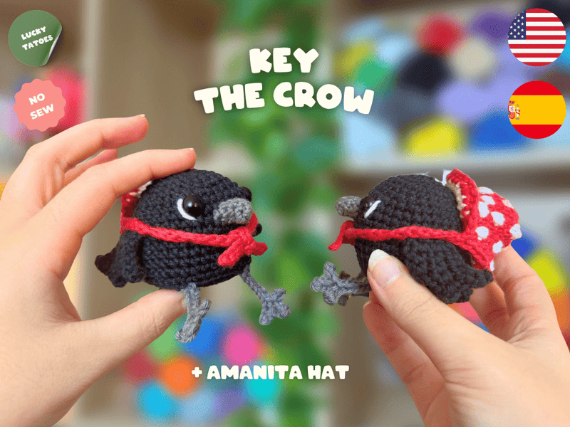 Two small crocheted crow characters wearing purple witch hats with yellow bands are held in human hands against a colorful blurred background. Text reads 'KEY THE CROW' and '+ WITCH HAT', with 'LUCKY TATTOO' and 'NO SEW' badges plus US and Spain flags.