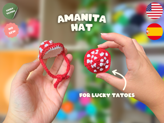 A pair of hands holding a small red and white crocheted amanita mushroom hat, with text overlays reading 'AMANITA HAT' and 'FOR LUCKY TATOES', plus 'LUCKY TATOES' and 'NO SEW' badges and US/Spain flags.