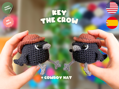 Two hands holding small crocheted crow toys wearing cowboy hats, with text reading 'KEY THE CROW' and 'WITCH HAT' on a colorful blurred background. Flags for USA and Spain and badges for 'Lucky Tattoos' and 'No Sew' appear in the corners.